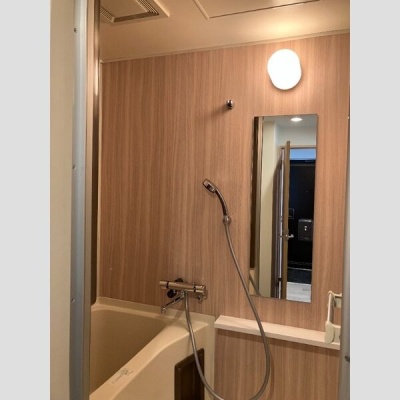 木目調パネルが印象的な浴室。シャワーと鏡を備えています。